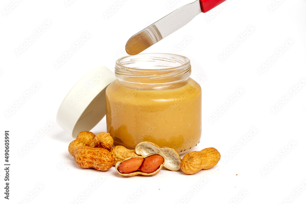 Glass and knife with peanut butter on white background with peanuts around Glass and knife with peanut butter on white background with peanuts around