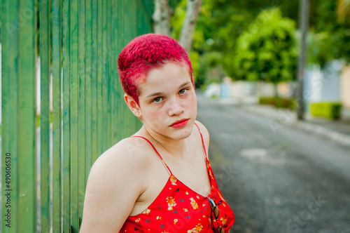 Portrait of young woman on a green metal fence. Portrait of young girl with red dyed hair
