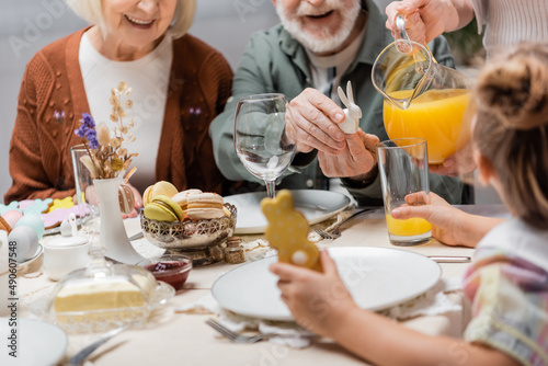 cropped view of woman pouring orange juice near family having easter dinner.