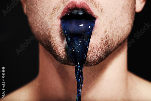 The colour of lies. Closeup of a young mans mouth spitting out purple liquid. photo