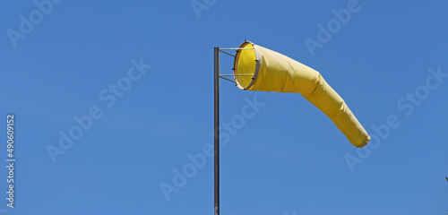Yellow windsock on a pole with a blue sky background. photo