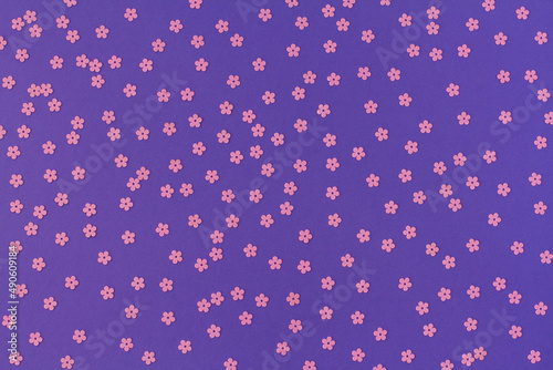 Scattered random pink sequins in form of flowers on purple textured background