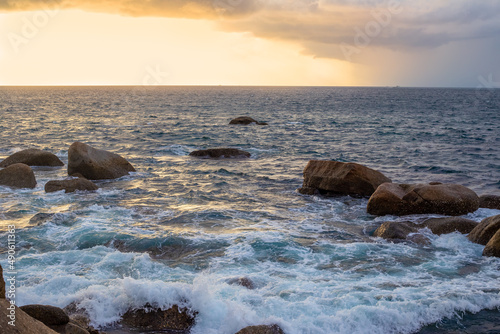 Stormy boiling sea with a rocky shore at sunset. Maritime dramatic landscape