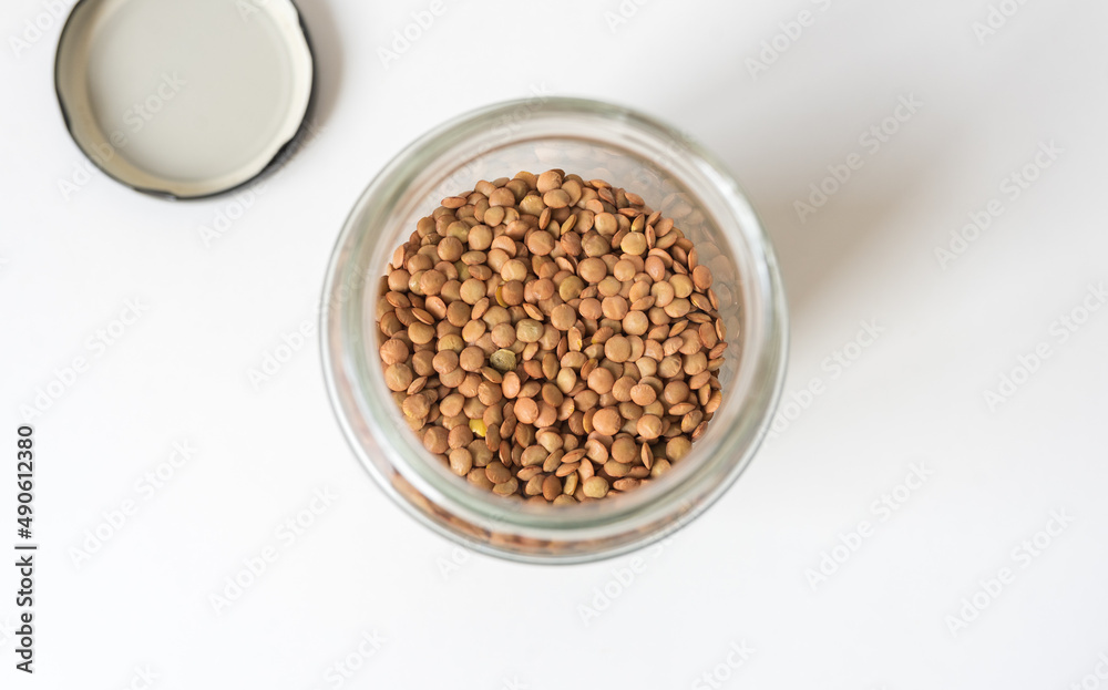 High angle closeup of brown lentils in glass jar on white background (selective focus) High angle closeup of brown lentils in glass jar on white background (selective focus)