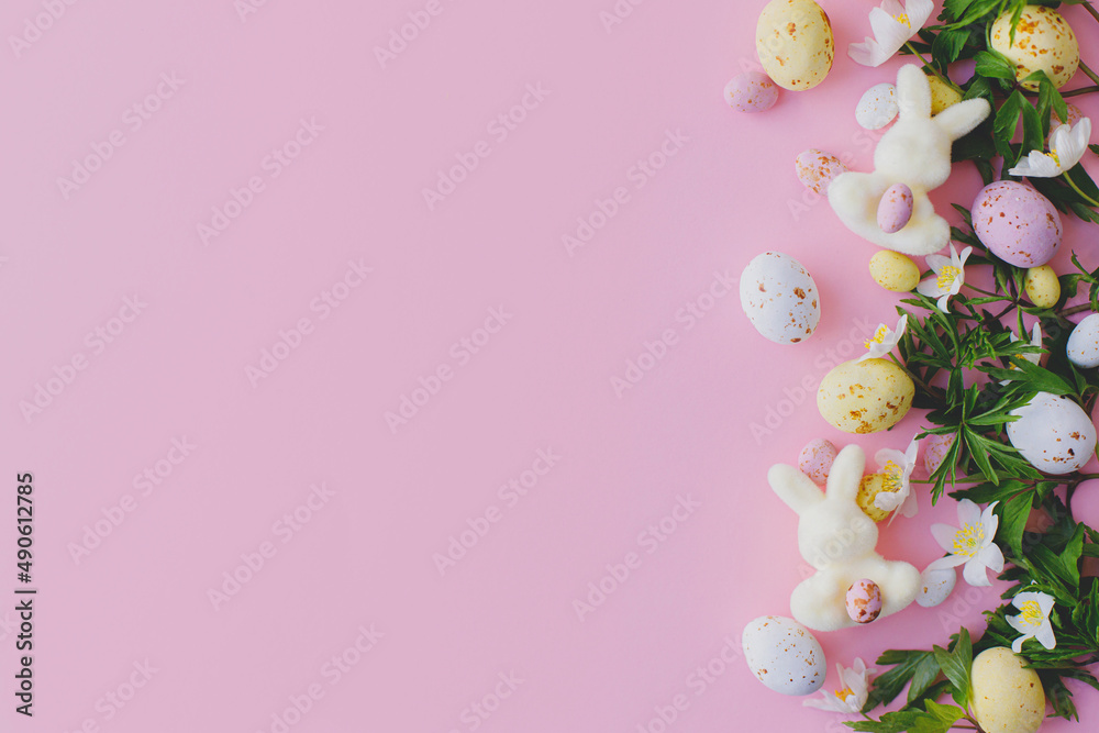 Happy Easter! Colorful Easter chocolate eggs, bunnies and spring flowers border flat lay on pink background. Stylish easter layout. Greeting card or banner template