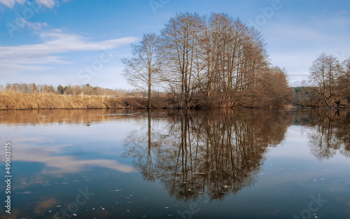 Spring landscape in early spring. River, trees without leaves, reflection in the water