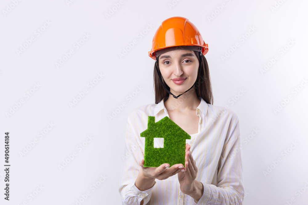 A young girl architect in a construction helmet demonstrates a model of a green house. Sale of ecological real estate. A young girl architect in a construction helmet demonstrates a model of a green house. Sale of ecological real estate.