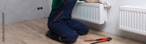 A male plumber installs a radiator in the heating system of an apartment. The guy contacts the service by phone. photo