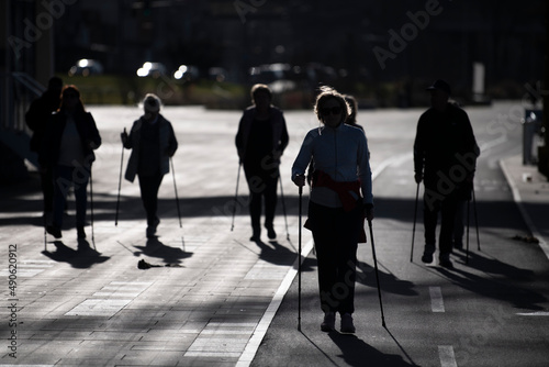Large group of Senior people making nordic walking by river on promenade. Elderly people walking with scandinavian sticks on beautiful sunny day. 05.01.2022 Belgrade, Serbia