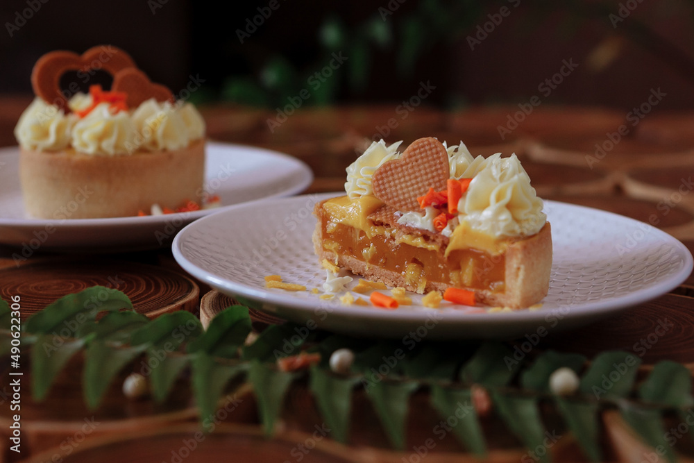 dessert, cheesecake with mango and passion fruit in the form of brownies with mousse on top. Decorated with cookies in the form of a heart. On a wooden table in a white plate dessert, cheesecake with mango and passion fruit in the form of brownies with mousse on top. Decorated with cookies in the form of a heart. On a wooden table in a white plate