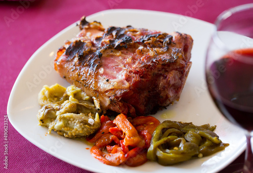 Delicious grilled pork knuckle with braised vegetables and glass of red wine..