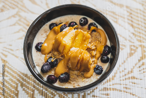 vegan soy milk oatmeail with peanut butter mango and blueberries topping, healthy plant-based food