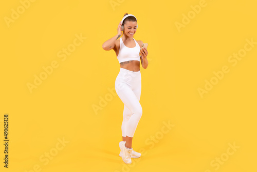 sport woman with headphones and smartphone on yellow background. full length