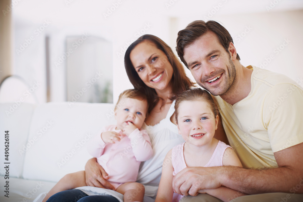 Proud parents of two beautiful daughters. Portrait of a happy family of four sitting together on a sofa indoors.
