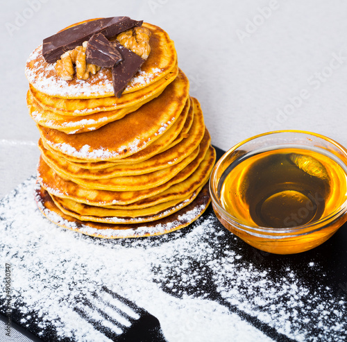 Stack of tasty pancakes served with honey, chocolate and powdered sugar at plate