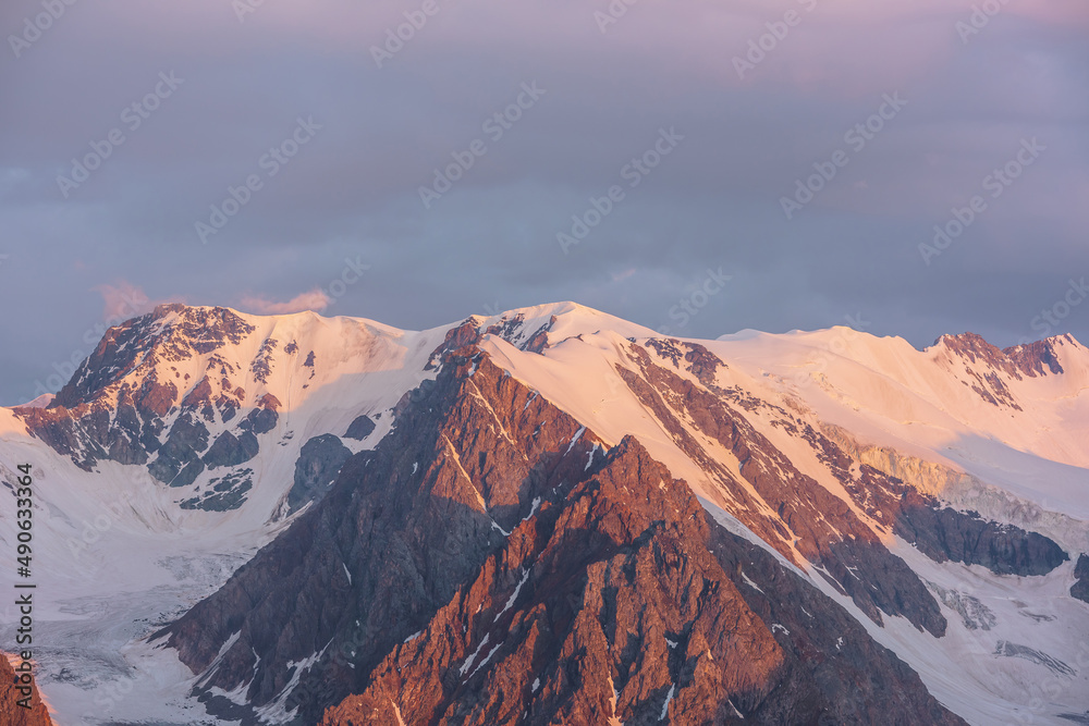 Scenic aerial view to high snow mountains in early morning at dawn. Awesome scenery with sunlit gold mountains in cloudy sky at sunrise. Morning landscape with snow mountain range in golden sunlight.