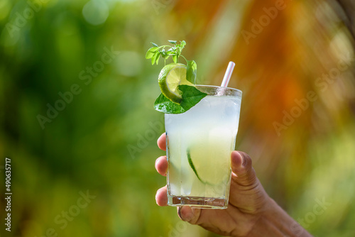 Brazilian drink caipirinha. Hand holding a caipirinha drink with blurred foliage in the background. photo