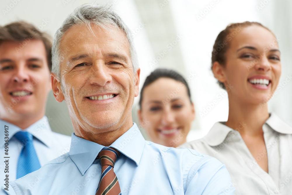 Closeup of senior businessman with his team in background. Closeup of successful senior businessman with his team in background smiling. Closeup of senior businessman with his team in background. Closeup of successful senior businessman with his team in background smiling.