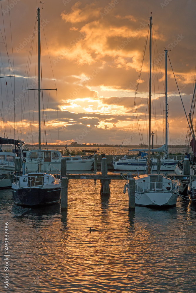 A vivid sunset over a harbor creates a blaze in the sky  that is reflected on the water.