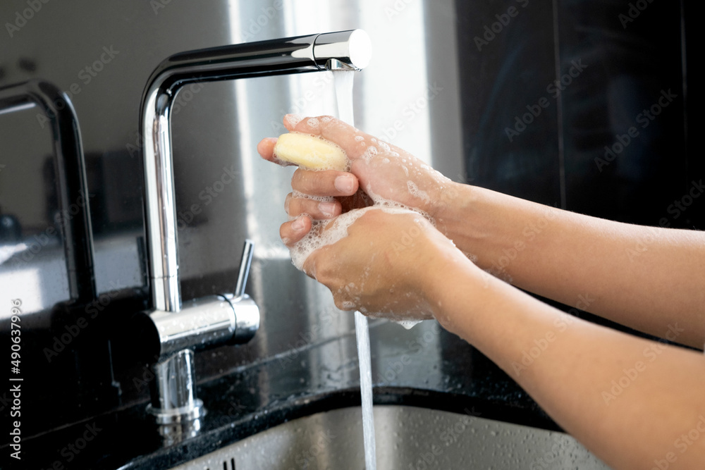 Hands of woman wash their hands in a sink with foam to wash the skin and water flows through the hands. Concept of health, cleaning and preventing germs and coronavirus from contacting hands