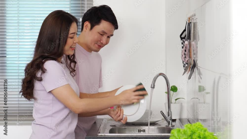 happy young couple washing dishes together in the sink in the kitchen at home happy young couple washing dishes together in the sink in the kitchen at home