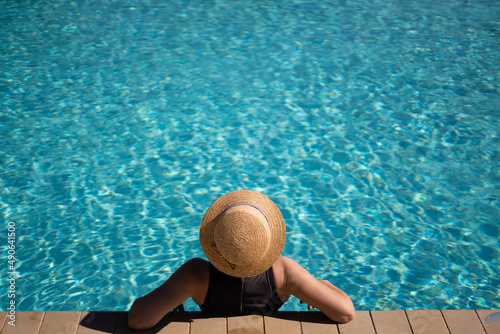 young beautiful unrecognizable woman in a straw hat is resting during a vacation in the pool.