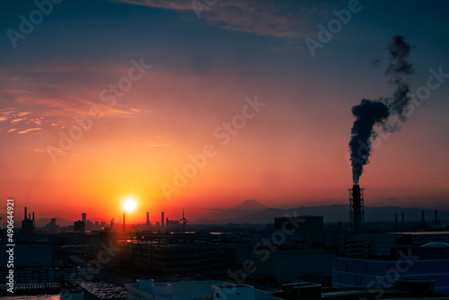 夕焼けに染まる富士山と工場の煙突からの煙