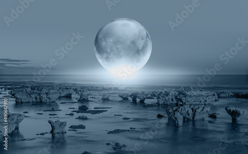 Full glass moon (or crystal ball moon) rising over empty sea with rock at night 