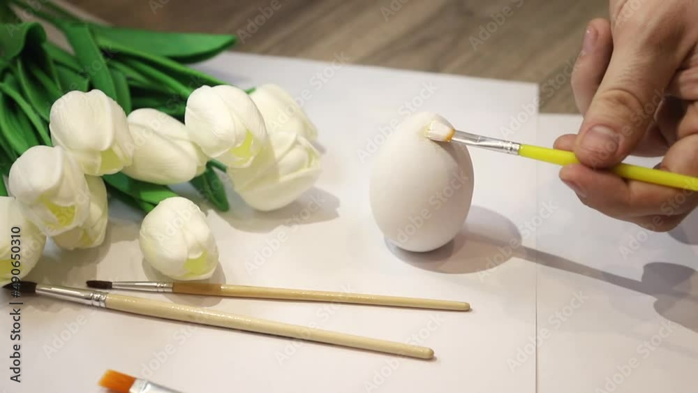 Close-up. Hands paint the Easter egg with a brush pink on a white background. Holiday concept Close-up. Hands paint the Easter egg with a brush pink on a white background. Holiday concept