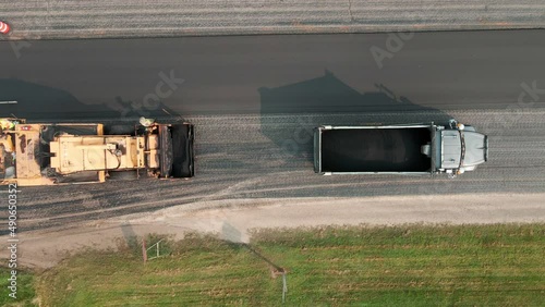 Birds eye view of blacktop paver working slowly across the road laying new blacktop. Dump truck full of aggregate material for the road. Crew working together. 