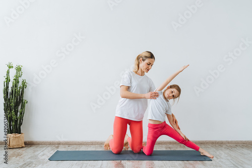 A woman helps a girl build a pose out of yoga. Paired yoga with an instructor. Yoga classes with your child. Balance and tranquility. Bright Yoga Studio