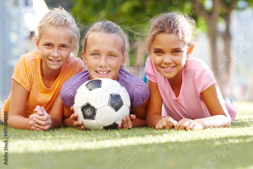 Our school offers girls soccer. Three smiling girls lying on some sunny grass posing with a soccer ball- copyspace.