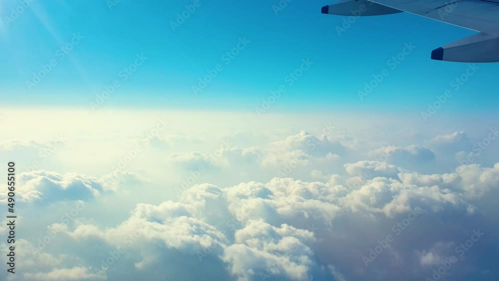 Airplane wing passing above thick blanket of white clouds, mid-air. Window view.
