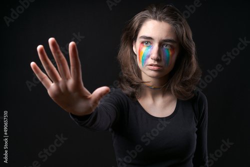 Flag LGBT lizbian woman with rainbow tears on her cheek defends herself with her hands in front of her on a black background. The girl is scared for their sexual orientation. Discrimination concept photo