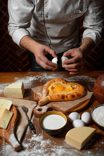 Close-up on Caucasian flatbread Ajarian khachapuri with egg and butter on a wooden board in the shape of a heart, a large piece of cheese photo