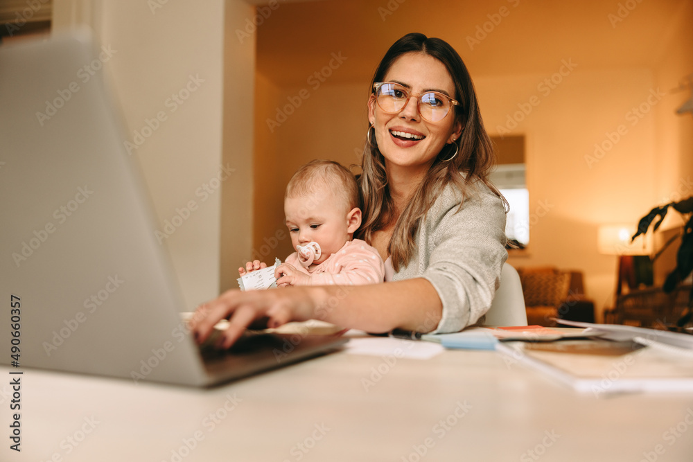 Happy single mom typing on a laptop in her home office Happy single mom typing on a laptop in her home office