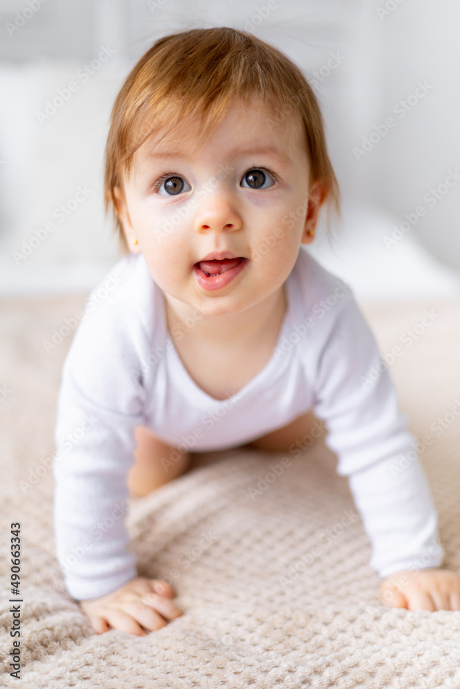 a small child girl learns to crawl on a bed in a bright room on cotton white linen, close-up portrait a small child girl learns to crawl on a bed in a bright room on cotton white linen, close-up portrait