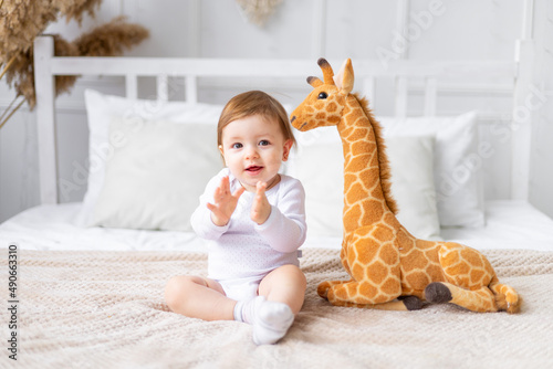 Canvas Print cute little baby girl with a stuffed giraffe toy is sitting on a bed with a brig