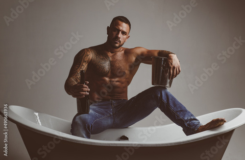 Sexy seductive muscular man sit on bathtub in bathroom, men holiday with champagne. Celebrating christmas or birthday. Private sex party.