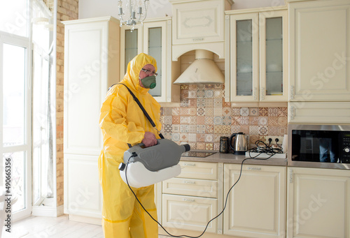 A man specialist in insect control in a yellow protective suit sprays the walls in the apartment protects against insects