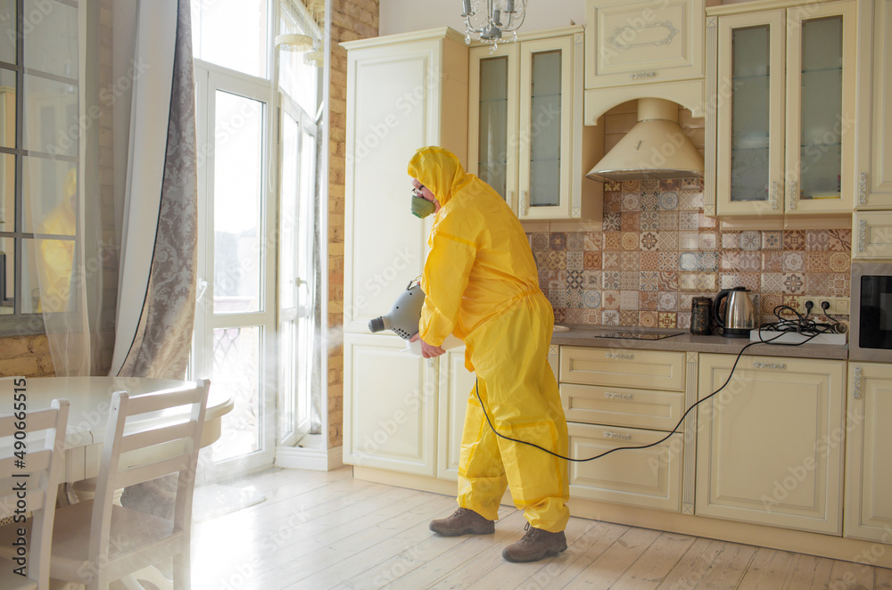A man, an insect control specialist, in a yellow protective suit sprays the walls in the apartment, protects against viruses. A man, an insect control specialist, in a yellow protective suit sprays the walls in the apartment, protects against viruses.