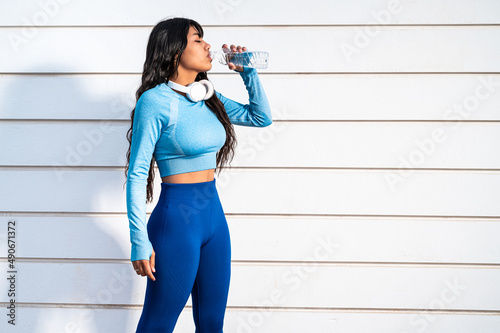 Atractiva mujer colombiana tomando un descanso para beber agua mientras hace deporte en un parque