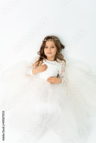 A little girl lying in a white dress and looking at the camera