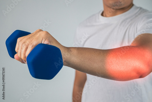 Tennis elbow concept. The man uses a blue dumbbell to physical therapy. Pain symptom area is shown with red color. Healthcare knowledge. Medium close up shot.