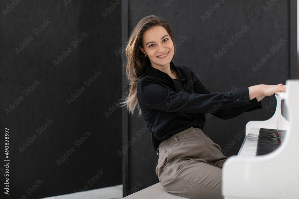 Portrait of a happy woman in a casual shirt playing the white grand piano on black background Portrait of a happy woman in a casual shirt playing the white grand piano on black background