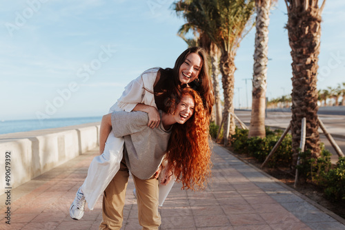 Quadro em tela Energetic young woman piggybacking her best friend in the promenade