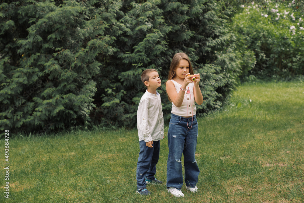 Brother and sister play with a children's camera in the park.