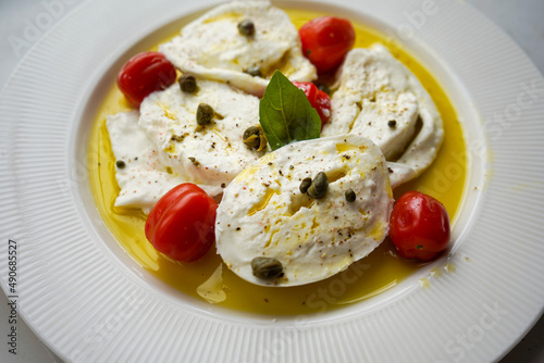 Horizontal flat lay of classic italian caprese salad with sliced tomatoes, mozzarella, basil, olive oil, pepper, salt and toast. Rustic mediterranean meal on light background