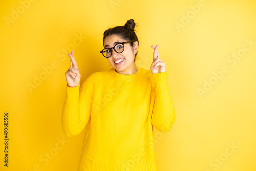 Young beautiful woman wearing casual sweater over isolated yellow background gesturing finger crossed smiling with hope and looking side