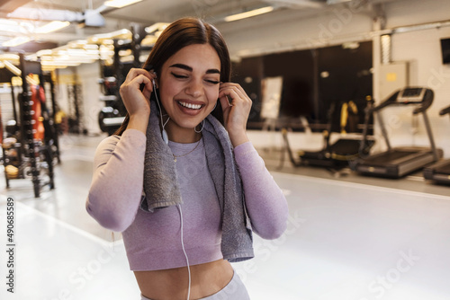 Shot of a young woman listening to music through earphones while at the gym. Photo of an attractive young woman standing in the gym and listening to music through earphones during her workout.